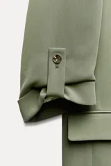 Blazer color blanco, abierta, con cuello solapa y hombreras. Manga tres cuartos acabada en vuelta con trabilla y botón dorado. Bolsillos delanteros con solapa.