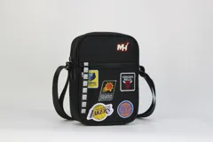 Morral cruzado negro con correa ajustable. Presenta múltiples parches bordados de equipos de la NBA (Memphis Grizzlies, Phoenix Suns, Chicago Bulls, Los Angeles Lakers, New York Knicks) y una cinta lateral con el logo NBA repetido.