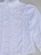 Blusa blanca con cuello alto con volados, mangas largas abullonadas y bordado calado.