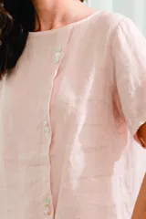 Blusa blanca de lino, corte holgado, con cuello redondo y cierre frontal con botones.