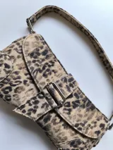 Cartera tipo baguette con estampado animal print, cierre superior con solapa y hebilla decorativa.