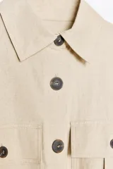 Camisa color marrón con cuello solapa y manga larga acabada en vuelta con trabilla y botón. Bolsillos delanteros de plastrón con solapa. Bajo con aberturas laterales. Cierre frontal con botones y cinturón de la misma tela.