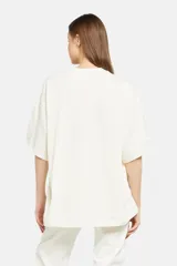 Remera color crema de corte holgado con cuello redondo y mangas cortas. Presenta un estampado floral en tonos beige y marrón a lo largo del frente y la manga derecha.