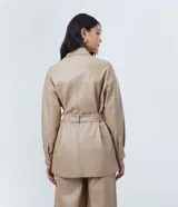 Campera de poliuretano (PU) color beige, con cuello camisa, cierre frontal de botones y dos bolsillos con solapa en el pecho. Incluye un cinturón ajustable con hebilla redonda forrada al tono.