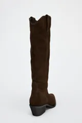 Bota alta de caña alta color marrón chocolate, de serraje con puntera fina y taco bajo.