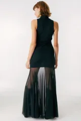 Vestido largo color beige, con cuello alto y sin mangas. La parte superior es ajustada al cuerpo y la falda es amplia y fluida, con paneles traslúcidos.