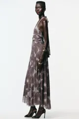 Vestido largo de tul con estampado floral en tonos marrón y celeste, cuello halter con lazada, escote pico cruzado, aberturas laterales en la cintura, frunces en la falda y forro interior.