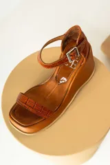 Sandalias de cuero color marrón con plataforma y taco de cuña. Tiras anchas con textura tipo cocodrilo y hebilla metálica plateada.