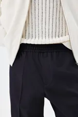 Pantalón tobillero azul marino de sarga suave con cintura elástica y cordón ajustable. Tiene bolsillos laterales y traseros ribeteados, piernas con pliegues cosidos y doblez en el bajo.