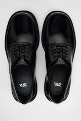 Zapato tipo mocasín negro acharolado con punta redonda y cierre de cordones. Suela de 4 cm de altura.