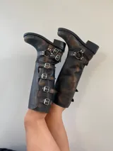 Botas de cuero gastado color marrón con hebillas y apliques de metal de caña alta.