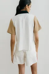 Camisa de manga corta color crudo con estampado de lunares negros, cuello clásico, cierre frontal con botones negros y dos bolsillos de parche en el pecho.