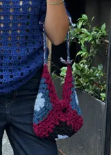 Cartera tejida a crochet, con diseño geométrico multicolor y asa corta.