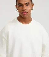 Remera color crema de corte amplio, con cuello redondo y mangas cortas con sisa desplazada. Confeccionada en algodón y poliéster.