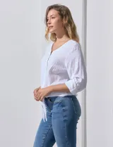 Blusa de algodón a rayas verticales finas en tonos blanco y lila, con escote en V, abertura frontal con botones y mangas largas regulables con presilla y botón. El ruedo termina anudado al frente.