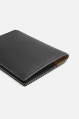 Cartera negra para pasaporte fabricada en piel, con tres posiciones para tarjetas y dos ranuras laterales.