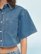 Camisa de manga corta color celeste, con cuello clásico, cierre frontal con botones y bolsillo de parche en el pecho.