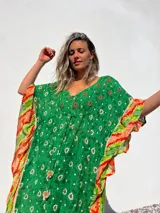 Túnica corta verde con estampado de flores blancas y detalles bordados en el escote. Mangas anchas con terminación en tela estampada a rayas naranjas y blancas.