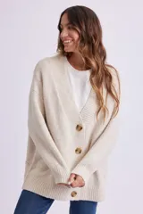 Cardigan de punto color crema, con escote en V, cierre frontal con botones marrones y corte holgado.