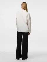 Camisa blanca de corte holgado, con cuello clásico, mangas largas con puños abotonados y cierre frontal con cremallera.