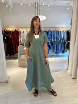 Vestido largo verde musgo de corte acampanado, con mangas cortas, cuello en V y detalle de picos desiguales en el ruedo. Incluye bolsillos laterales.