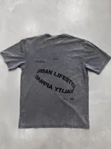 Remera de manga corta color gris oscuro con efecto acid wash. Presenta un estampado curvo en la espalda con texto en inglés que incluye las frases "URBAN LIFESTYLE" y "QUALITY APPAREL", junto con el logo de la marca "OSTEN".