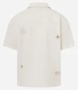 Camisa de hombre con corte boxy, cuello inglés y abotonado delantero. Es de color crema y presenta bordados sutiles de motivos veraniegos en tono naranja claro.