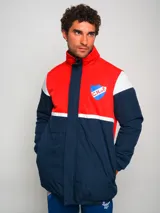 Campera parka de hombre con cuello alto, cierre frontal con cremallera y broches a presión, y escudo del Club Nacional de Football en el pecho. Diseño a bloques de color azul marino, blanco y rojo.