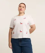 Blusa blanca de algodón con cuello redondo, manga corta abullonada y estampado de cerezas.