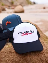 Gorra con visera Rusty, con frente blanco y logo bordado en negro y rojo, malla trasera negra y visera negra.