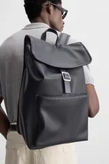 Mochila negra de cuero sintético, con solapa y cierre magnético. Tiene un compartimento principal con espacio para dispositivos electrónicos de hasta 13 pulgadas y un bolsillo con cierre. En la parte frontal cuenta con un bolsillo con cierre. Tiene asa de mano y dos asas de hombro ajustables y acolchadas.
