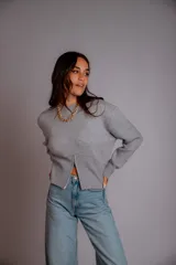 Buzo gris de punto con cuello redondo, mangas largas abullonadas y cierre frontal asimétrico.