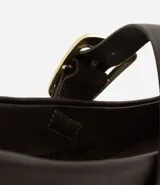 Zapatilla tipo bailarina de cuero color marrón, con punta redondeada y tira sobre el empeine con hebilla metálica dorada. Posee un tacón bajo de 1 cm y diseño clásico.