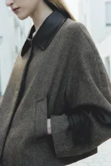 Chaqueta corta de tweed gris con cuello solapa y puños de cuero negro. Cierre frontal con botones ocultos.