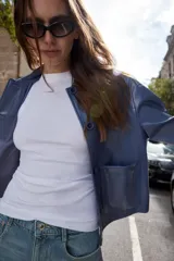 Cazadora azul de cuello solapa y manga larga. Tiene bolsillos de parche en el delantero y cierre frontal con botones.