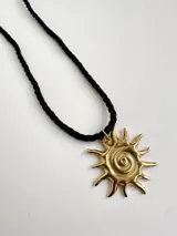 Collar con dije dorado en forma de sol con espiral en el centro, y tiento sailor negro.