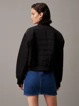 Campera bomber acolchada negra Calvin Klein, con logo bordado en el pecho y el puño. Confeccionada con poliéster reciclado, cuello, puños y bajo de canalé, cierre de cremallera, bolsillos con botón de presión en la cintura y forro ligeramente acolchado.