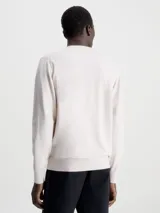 Sweater color beige de Calvin Klein, confeccionado en mezcla de tencel con elasticidad añadida. Tiene cuello redondo, puños y bajo de canalé, y etiqueta con logo de Calvin Klein por encima del bajo.