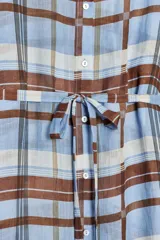 Vestido camisero midi de Zara Woman Collection, confeccionado en ramio 100%. Diseño a cuadros en tonos celeste, marrón y blanco. Cuello solapa, manga larga con puños, cinturón ajustable con lazadas y bajo asimétrico con aberturas laterales. Cierre frontal con botones.