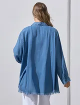 Camisa de jean celeste, marca Hester & Orchand, de corte oversize con cuello con solapa, escote en V y abertura central con botones. Delantera con bolsillos aplicados, mangas largas regulables con presilla y botón, y ruedo desflecado.