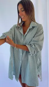 Camisa oversize a rayas verticales azules y blancas, con cuello clásico y cierre frontal con botones.