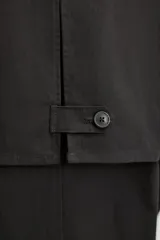 Trench corto negro confeccionado en tejido técnico ligero, con cuello con solapas de muesca, manga larga y cierre frontal de botonadura cruzada.