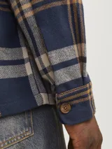 Sobrecamisa a cuadros azul marino, beige y ocre, de manga larga con puños abotonados, cierre frontal con botones y dos bolsillos de parche en el pecho.