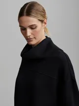 Buzo negro de corte oversize con cuello alto, mangas abullonadas, cierre lateral y hombros caídos.