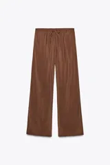 Pantalón marrón de tejido fluido, tiro medio, cintura elástica ajustable con cordones, bolsillos laterales y falsos bolsillos de vivo en la espalda.