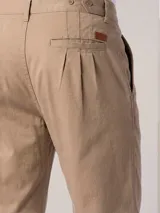 Pantalón de vestir color beige con pinzas, bolsillos laterales y traseros. El ruedo tiene un pequeño corte lateral.
