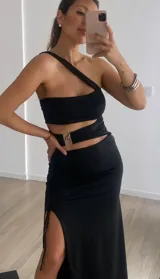 Vestido largo negro con abertura lateral, top asimétrico con un solo tirante y abertura en la cintura con hebilla dorada.