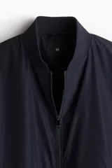 Campera bomber azul marino con cuello elevado acanalado y cierre frontal. Tiene bolsillos laterales y un bolsillo interior, todos con cierre. Los puños y el bajo son acanalados. Está forrada.