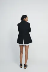 Blazer negra de corte clásico, con cuello de solapa y escote en pico. Tiene mangas largas con hombreras, bolsillos con solapa en el delantero y un bolsillo de vivo en el pecho. Está forrada y se cierra con un botón frontal.