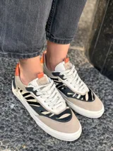 Championes urbanos de cuero vacuno color beige con estampado animal print en negro y blanco, detalles en naranja y suela blanca con plataforma.
